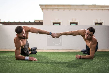Foto de Dos hombres guapos sin camisa dando golpe de puño después de un entrenamiento exitoso en el gimnasio de la azotea - Imagen libre de derechos