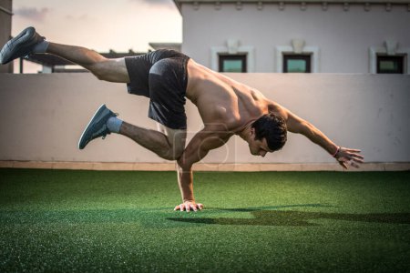 Téléchargez les photos : Jeune homme athlétique équilibrage tout en faisant une main pousser vers le haut et tenant son corps en l'air à l'extérieur - en image libre de droit