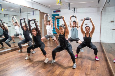 Foto de Grupo de deportistas haciendo ejercicio junto con placas de peso en el gimnasio - Imagen libre de derechos