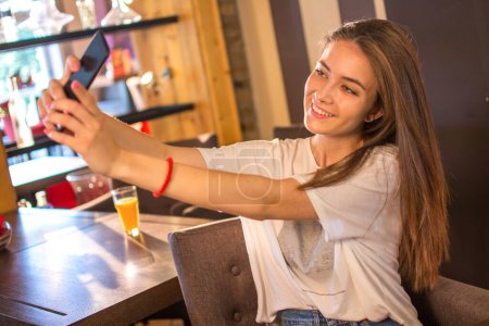 Téléchargez les photos : Adolescente utilisant le téléphone mobile pour faire l'autoportrait pour les réseaux sociaux - en image libre de droit