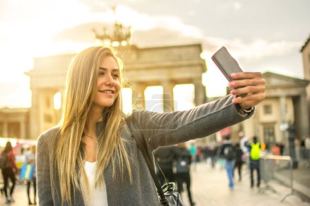Téléchargez les photos : Belle fille blonde prenant selfie devant la porte de Brandebourg dans la ville de Berlin, Allemagne - en image libre de droit