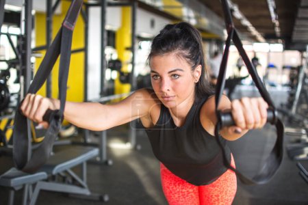 Téléchargez les photos : Jeune femme travaillant sur des bretelles de suspension dans la salle de gym - en image libre de droit
