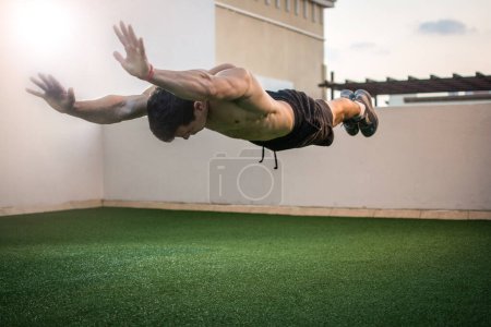 Photo for Young man with arms outstretched doing push ups with jumps on the rooftop building - Royalty Free Image