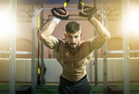 Foto de Hombre deportivo sin camisa haciendo ejercicio con correas de suspensión en el gimnasio - Imagen libre de derechos