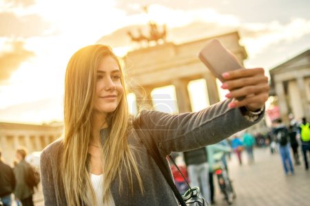 Téléchargez les photos : Belle fille aux cheveux blonds photographiant avec téléphone dans le centre-ville de Berlin - en image libre de droit