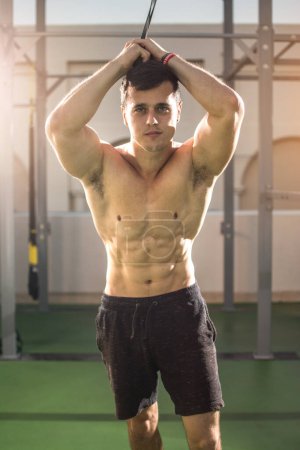 Téléchargez les photos : Portrait de jeune homme athlétique torse nu tenant la sangle et regardant la caméra dans la salle de gym extérieure - en image libre de droit