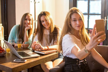 Foto de Tres chicas adolescentes lindas usando un teléfono móvil para tomar una foto en la cafetería - Imagen libre de derechos