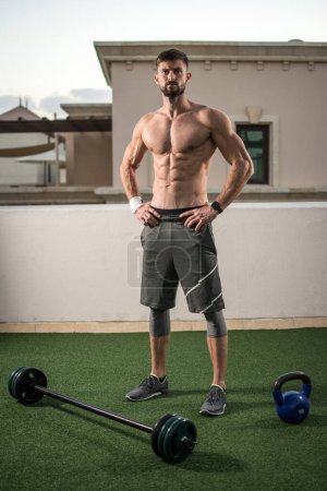 Foto de Retrato de cuerpo entero del hombre sin camisa atlético preparándose para el entrenamiento con pesas al aire libre - Imagen libre de derechos