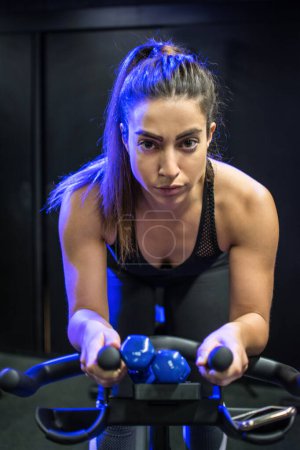 Téléchargez les photos : Portrait de femme fitness équitation vélo stationnaire dans la salle de gym - en image libre de droit