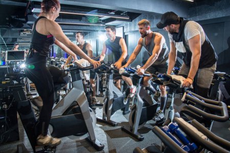 Téléchargez les photos : Groupe de personnes en vêtements de sport travaillant à un cours de vélo d'exercice dans la salle de gym - en image libre de droit
