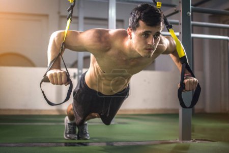 Foto de Guapo musculoso hombre de entrenamiento con correas de fitness trx en el gimnasio al aire libre - Imagen libre de derechos