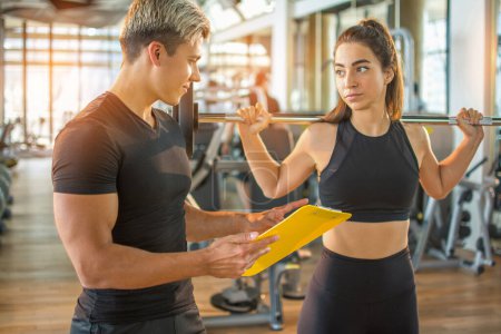 Photo for Male personal trainer and female client looking at progress date on clipboard at the gym. Young fit woman holding barbells and talking with personal trainer in gym. - Royalty Free Image