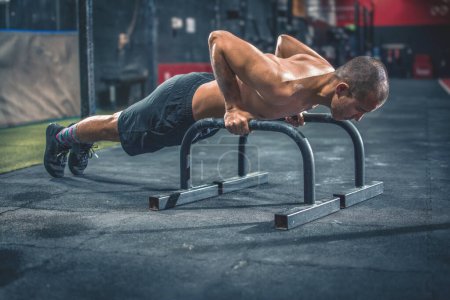 Fit et homme musclé faisant push-ups horizontaux avec barres parallèles dans la salle de gym