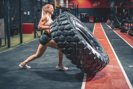 Photo for Fit blonde woman flipping heavy tire at gym - Royalty Free Image