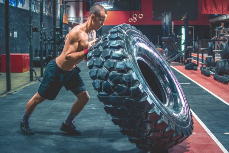 Foto de Un hombre sin camisa volteando neumáticos pesados en el gimnasio. Entrenamiento Crossfit - Imagen libre de derechos