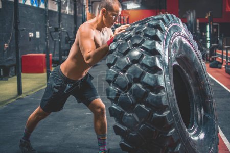 Photo for Shirtless man flipping heavy tire at gym - Royalty Free Image