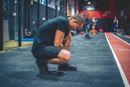 Foto de Vista lateral del deportista en forma atando cordones de zapatos, listo para entrenar en el gimnasio - Imagen libre de derechos