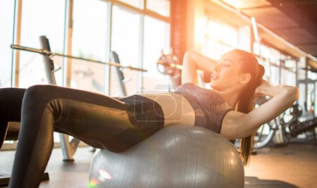 Foto de Atractiva mujer en forma haciendo abdominales en una pelota de fitness en el gimnasio - Imagen libre de derechos