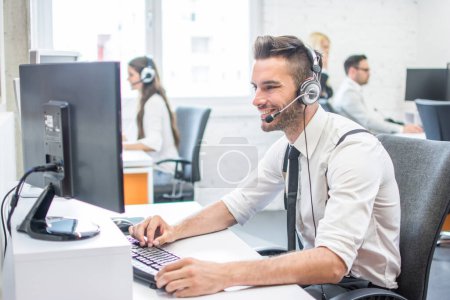 Téléchargez les photos : Bel homme en tenue de travail avec casque en utilisant l'ordinateur dans le centre d'appel - en image libre de droit