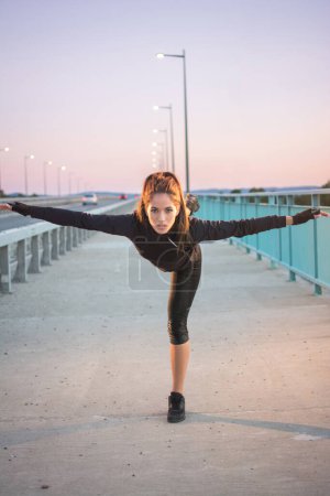Photo for Sporty girl balancing on one leg during evening training outdoors - Royalty Free Image