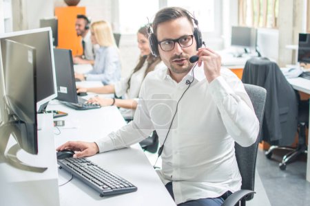 Photo for Call center operator with headset working in row with colleagues - Royalty Free Image