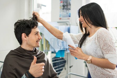 Foto de Feliz joven cliente masculino mostrando el pulgar a su peluquería femenina en el salón de belleza - Imagen libre de derechos