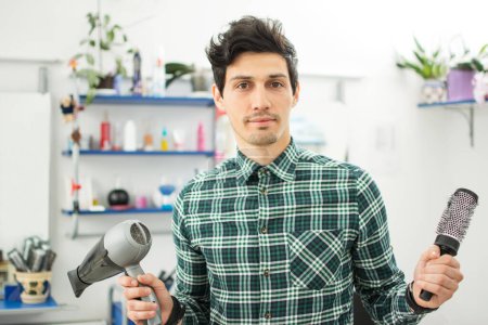Téléchargez les photos : Coiffeur professionnel masculin avec peigne et sèche-cheveux au salon de coiffure - en image libre de droit