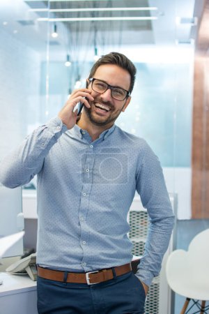 Téléchargez les photos : Joyeux jeune homme d'affaires parlant sur un téléphone portable dans le bureau - en image libre de droit