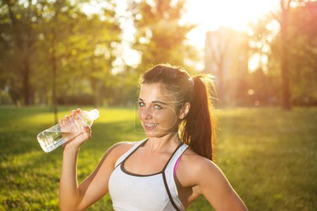 Thirsty fitness girl holding bottle of water in park