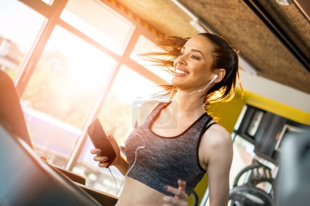 Photo for Young sporty woman athlete with smartphone running on treadmill in gym. - Royalty Free Image