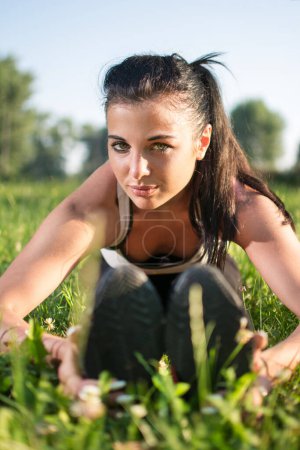 Photo for Beautiful woman doing gym stretches on the grass outdoors - Royalty Free Image