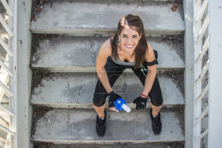 Téléchargez les photos : Au-dessus de la vue de la fille sportive avec bouteille d'eau relaxant sur les escaliers à l'extérieur - en image libre de droit