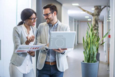 Photo for Tho smiling business people discussing document on laptop while standing in office hall - Royalty Free Image