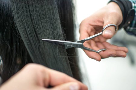 Téléchargez les photos : Homme styliste coupe pointes fourchues sur son client féminin avec des ciseaux au salon de coiffure - en image libre de droit