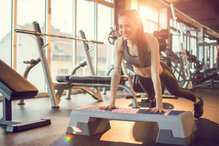 Photo for Young woman doing push-ups on exercise stepper in the gym. - Royalty Free Image