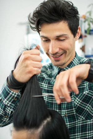 Foto de Joven peluquero masculino corte de pelo de los clientes con tijeras en el salón de belleza - Imagen libre de derechos
