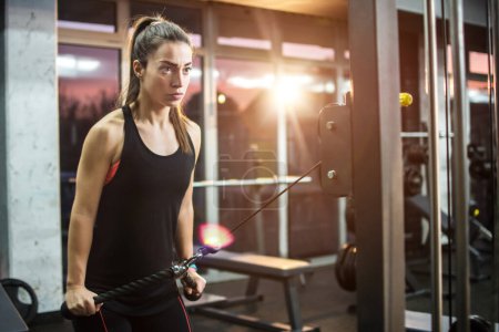 Junges sportliches Mädchen trainiert auf Abzugsgerät im Fitnessstudio