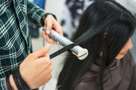 Primer plano de un peluquero alisando el pelo largo negro con planchas para el cabello