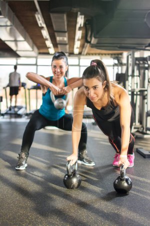 Two sporty girls doing exercises with kettlebells in gym