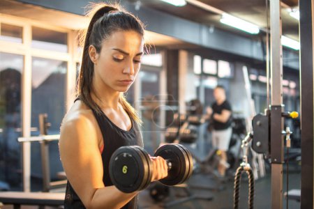 Téléchargez les photos : Athlétique jeune femme faire de l'exercice avec des poids dans la salle de gym - en image libre de droit