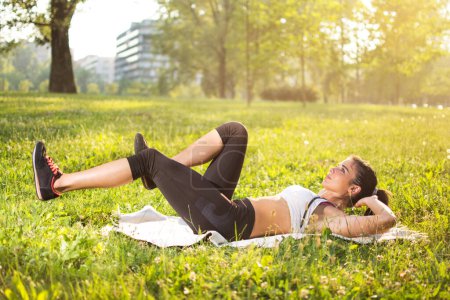 Foto de Fitness, deporte, entrenamiento, parque y concepto de estilo de vida - Mujer joven haciendo ejercicios en mientras que la alfombra al aire libre - Imagen libre de derechos