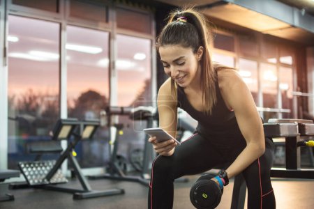 Téléchargez les photos : Jeune femme utilisant le téléphone dans la salle de gym - en image libre de droit