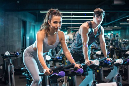 Foto de Mujer atractiva joven y hombre guapo haciendo ejercicio cardiovascular bicicletas de ciclismo en el gimnasio - Imagen libre de derechos