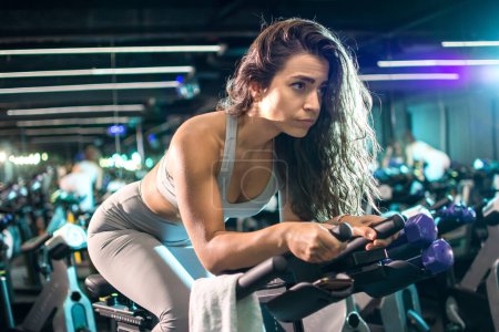 Photo for Beautiful fit woman cycling during workout on stationery bike for burning calories in the spinning studio - Royalty Free Image