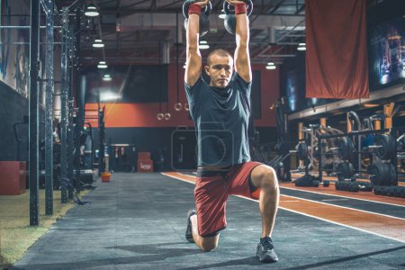 Photo for Fit young man lifting kettle bells above his head with strong movements in the gym - Royalty Free Image