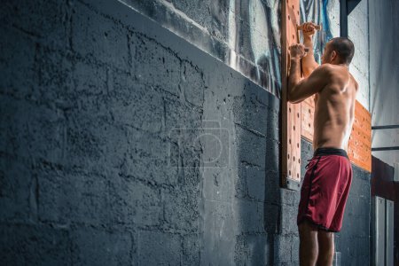 Téléchargez les photos : Homme athlétique torse nu grimpant sur un mur d'escalade en bois à la salle de gym - en image libre de droit