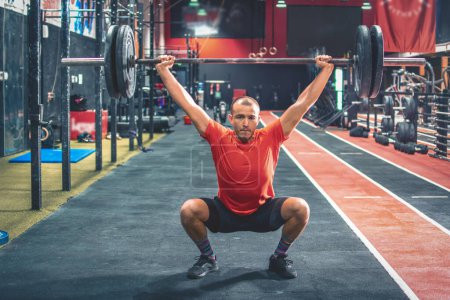 Junger fitter männlicher Sportler macht Kniebeugen mit einer Langhantel über den Schultern in einem Fitnessstudio