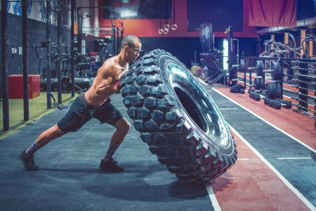 Photo for Shirtless man flipping heavy tire at gym - Royalty Free Image