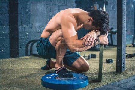 Téléchargez les photos : Jeune homme épuisement musculaire se reposant après un entraînement dur intense à la salle de gym - en image libre de droit