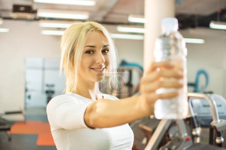 Foto de Joven rubia mostrando botella de agua en un gimnasio. - Imagen libre de derechos